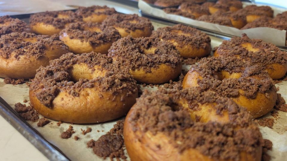 Ring-shaped bakes with a crumbly brown topping on a tray