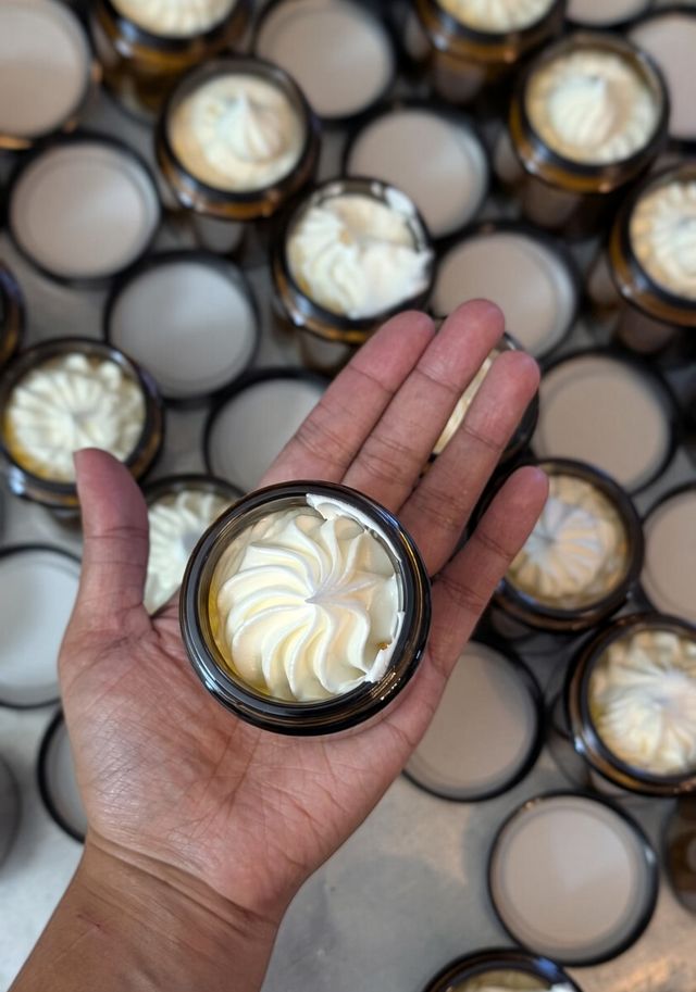 Hand holding an amber jar of whipped tallow above many filled jars
